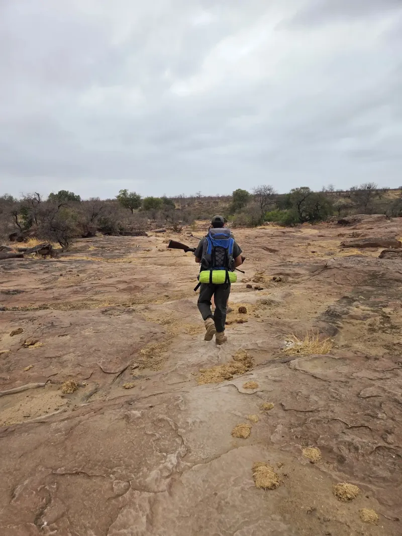 Armed guide hiking across rocky terrain with backpack